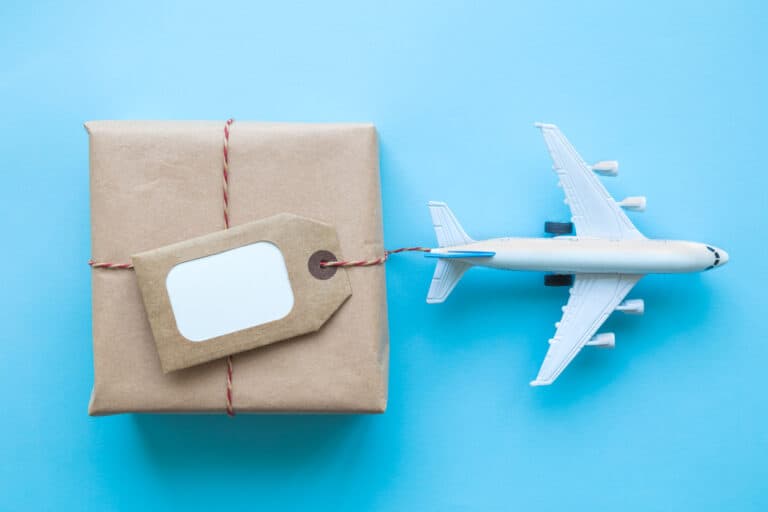 Flat lay of wrapped package with blank tag and airplane model on pastel blue background. Image represents global distribution and export and the importance of having a market development strategy.