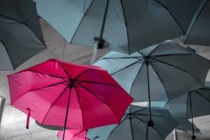 A pink umbrella amongst grey umbrellas to suggest differentiation and what a USP stands for in marketing.